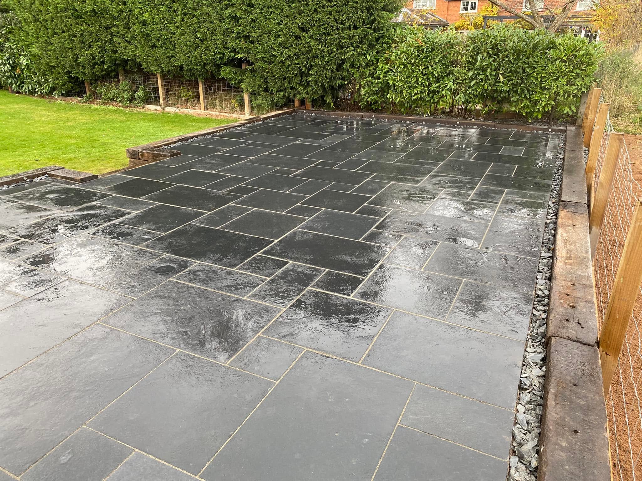 Dark stone patio with timber sleeper boundary — partners' past work