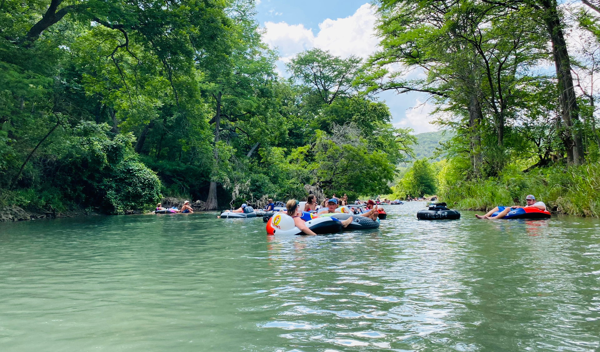 People floating in tubes down the spring-fed Guadalupe River past cypress trees near New Braunfels, Texas