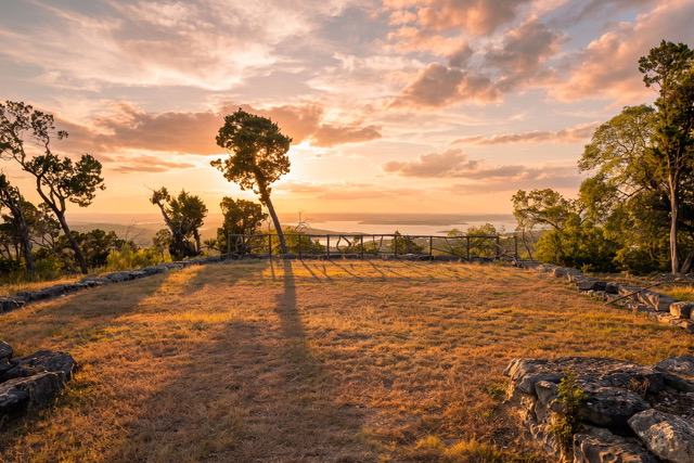 Warm golden hour sunset over the canyon lake meadow overlook with rustic cedar railing at The Point CLTX