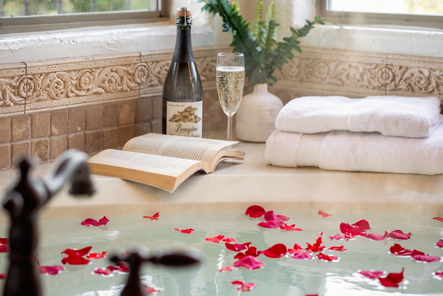Romantic bridal soaking tub with floating rose petals, chilled champagne, and carved stone surround at The Point CLTX