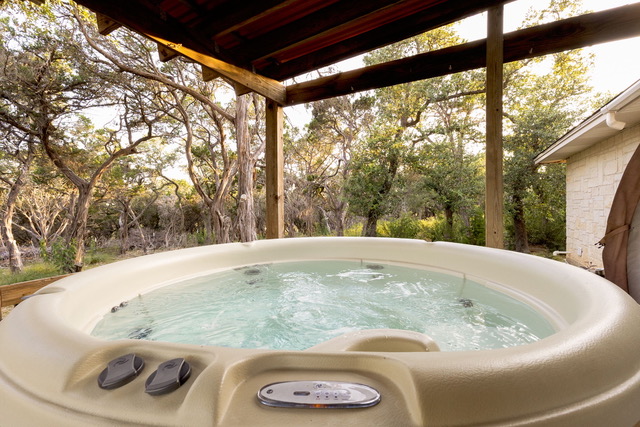Outdoor hot tub under covered timber arbor surrounded by Texas Hill Country trees and nature