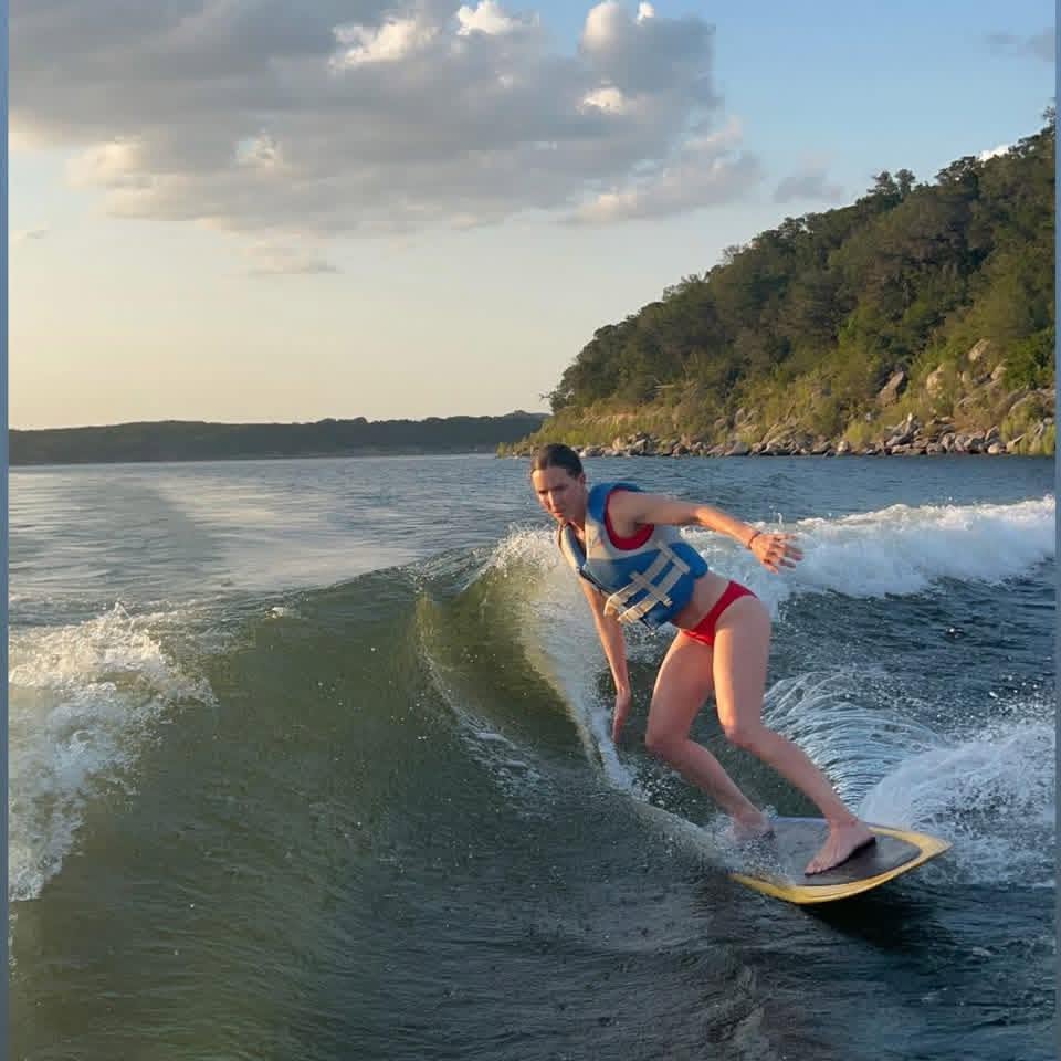 Wake surfing and wakeboarding on the clear waters of Canyon Lake, Texas against the wooded shoreline and open sky