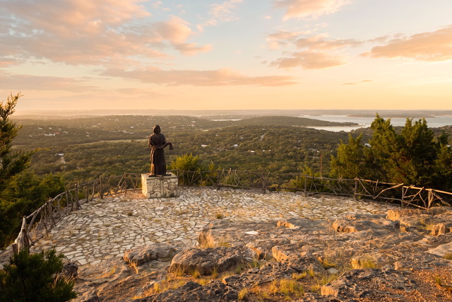 Stone sanctuary overlook with bronze statue gazing across Canyon Lake and the Texas Hill Country at sunrise, creating an inspiring setting for faith and worship retreats