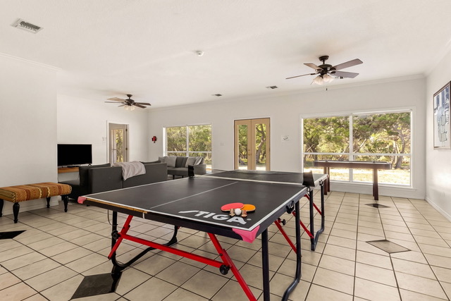 Sunlit game room and lounge featuring competition table tennis, television lounge, and picture windows looking out to Hill Country nature