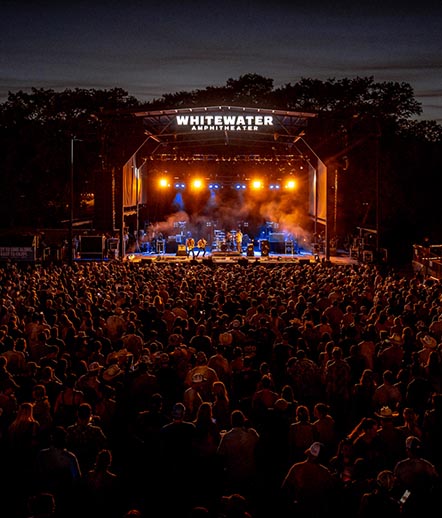 Live concert crowd at night illuminated by stage lights at Whitewater Amphitheater on the Guadalupe River in New Braunfels, Texas