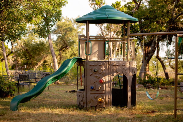 Children's playground playset with slide and swings under shaded oak trees for family reunions at The Point CLTX