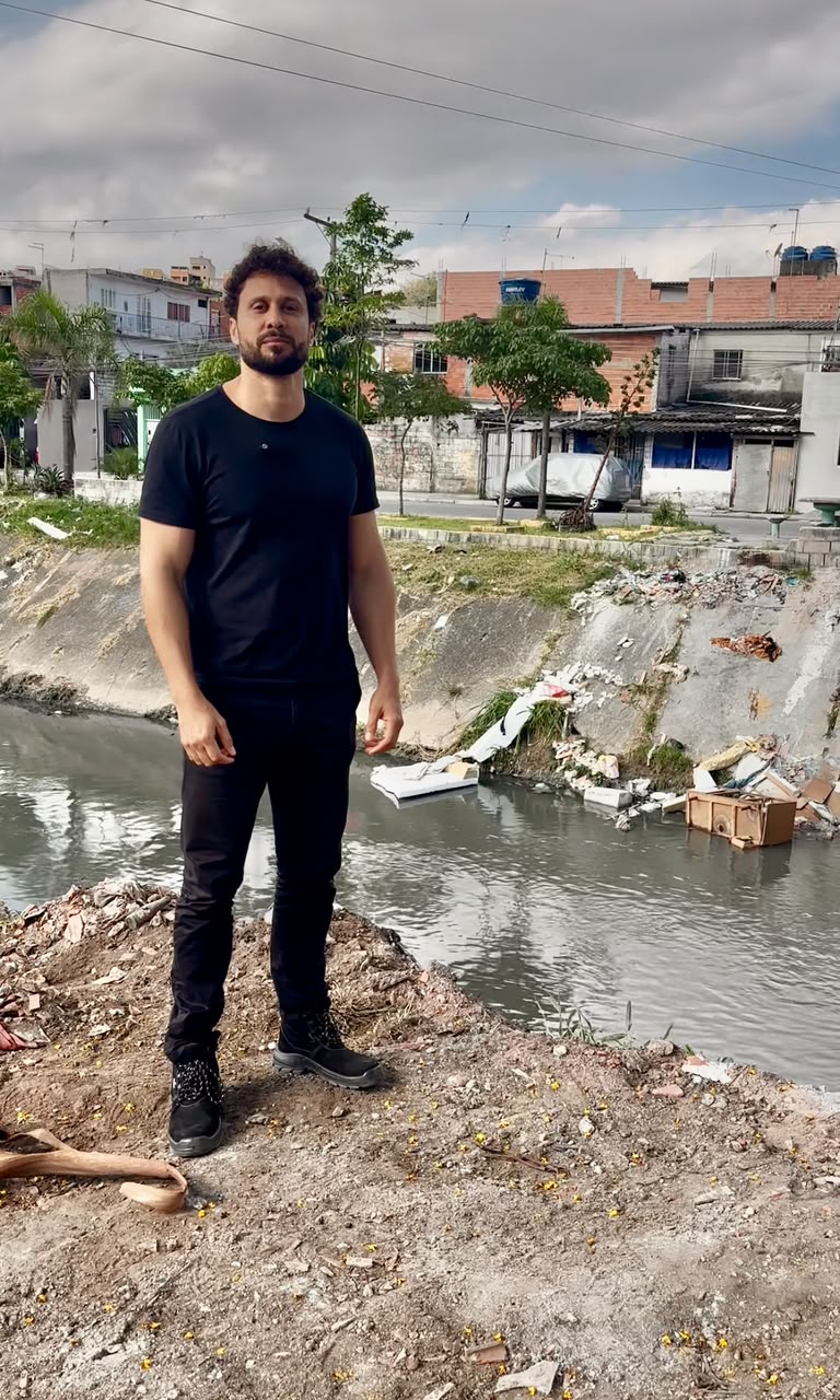 Diego Marinho em frente a canal de esgoto a céu aberto em área periférica