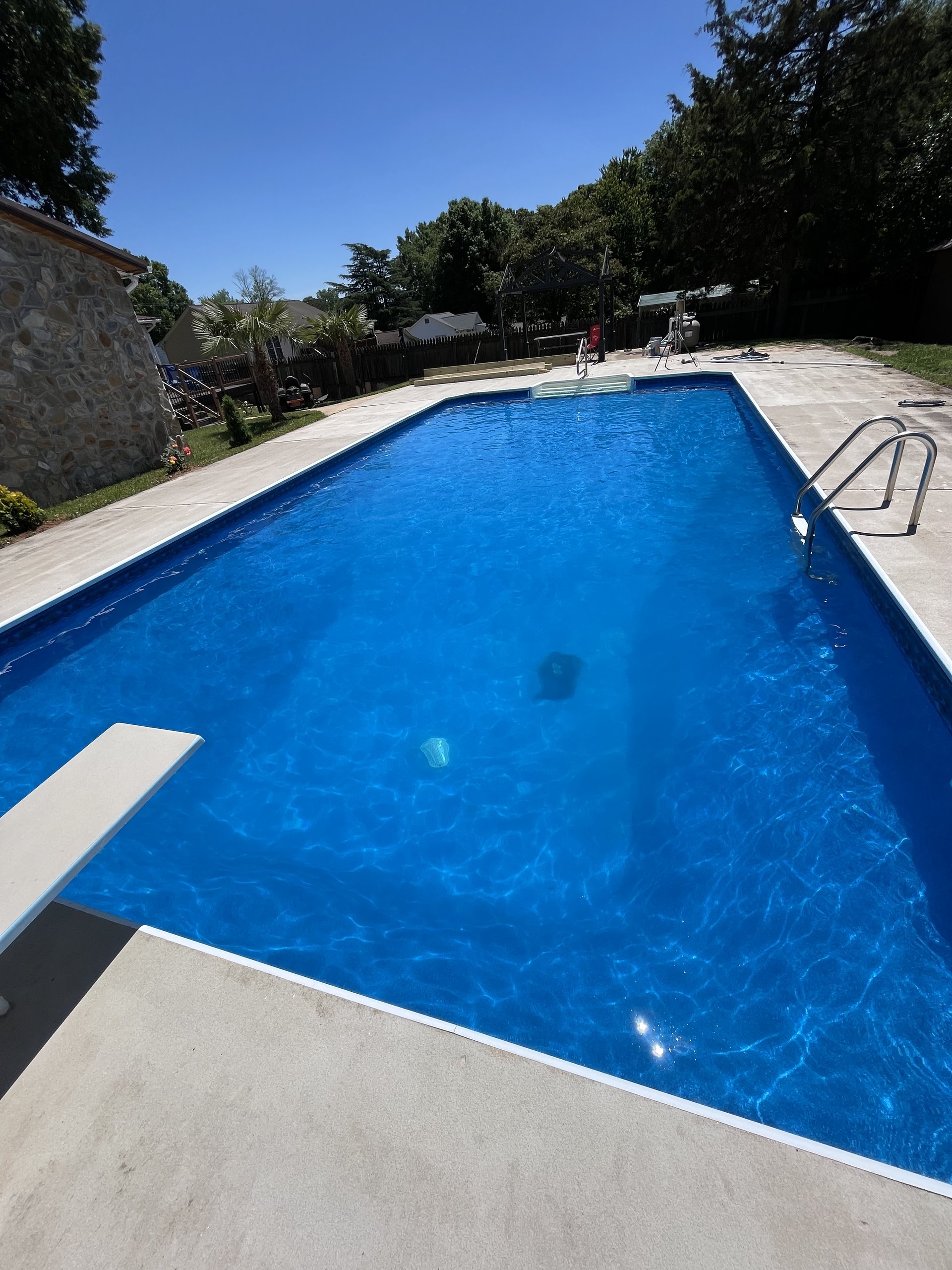 Crystal clear blue swimming pool with diving board and sunlit concrete deck