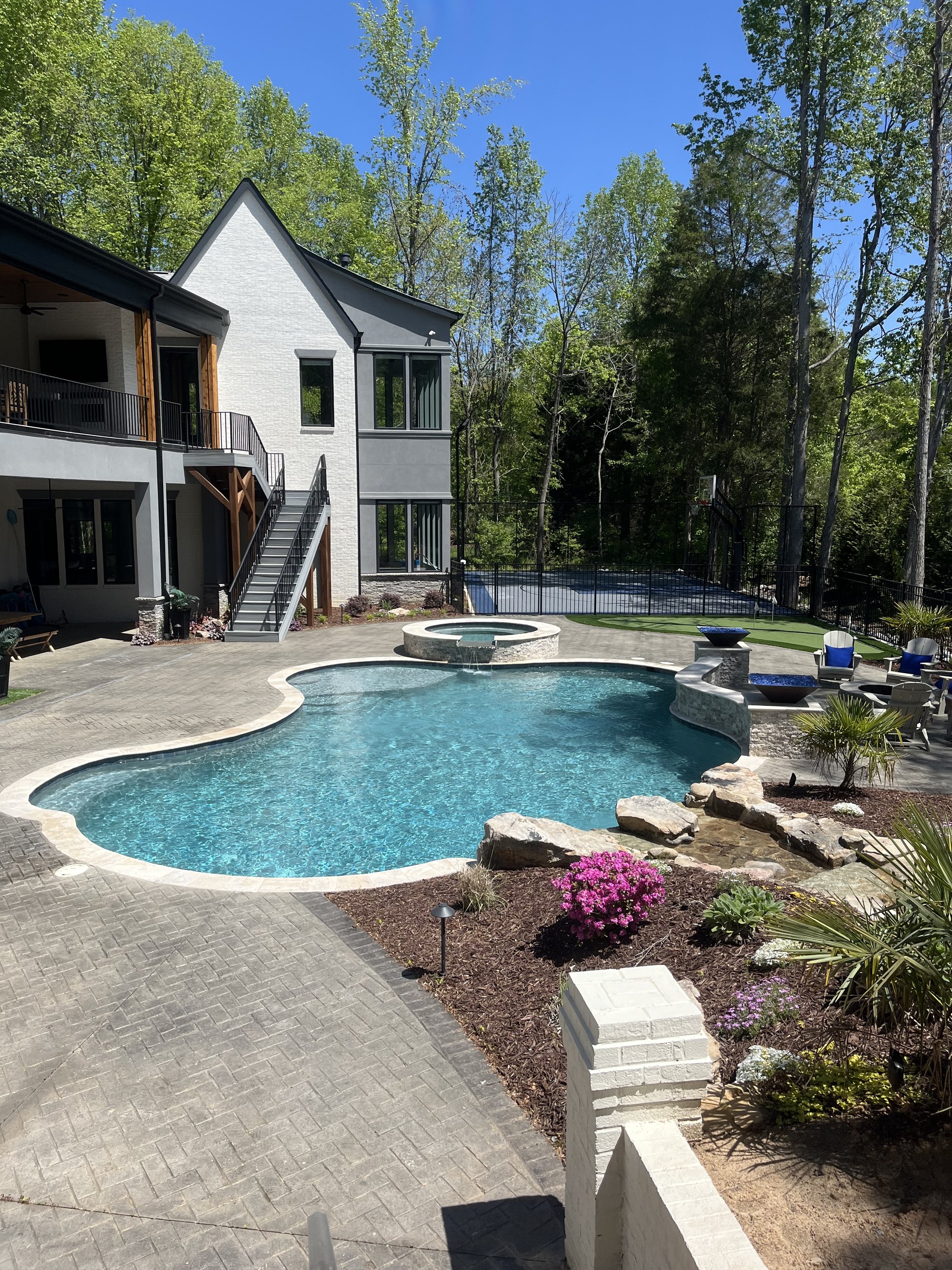 Custom backyard swimming pool and elevated spa with waterfall spillover, stone deck, and lush landscaped surroundings