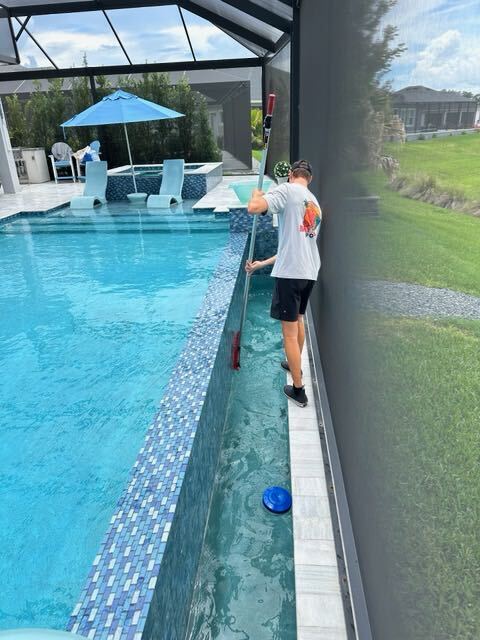 Baywatch Pools technician brushing pool tile and wall in screened enclosure