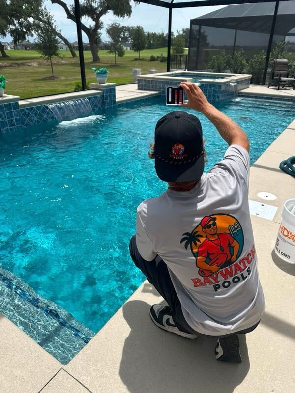 Baywatch Pools technician checking pool chemistry with test reader poolside