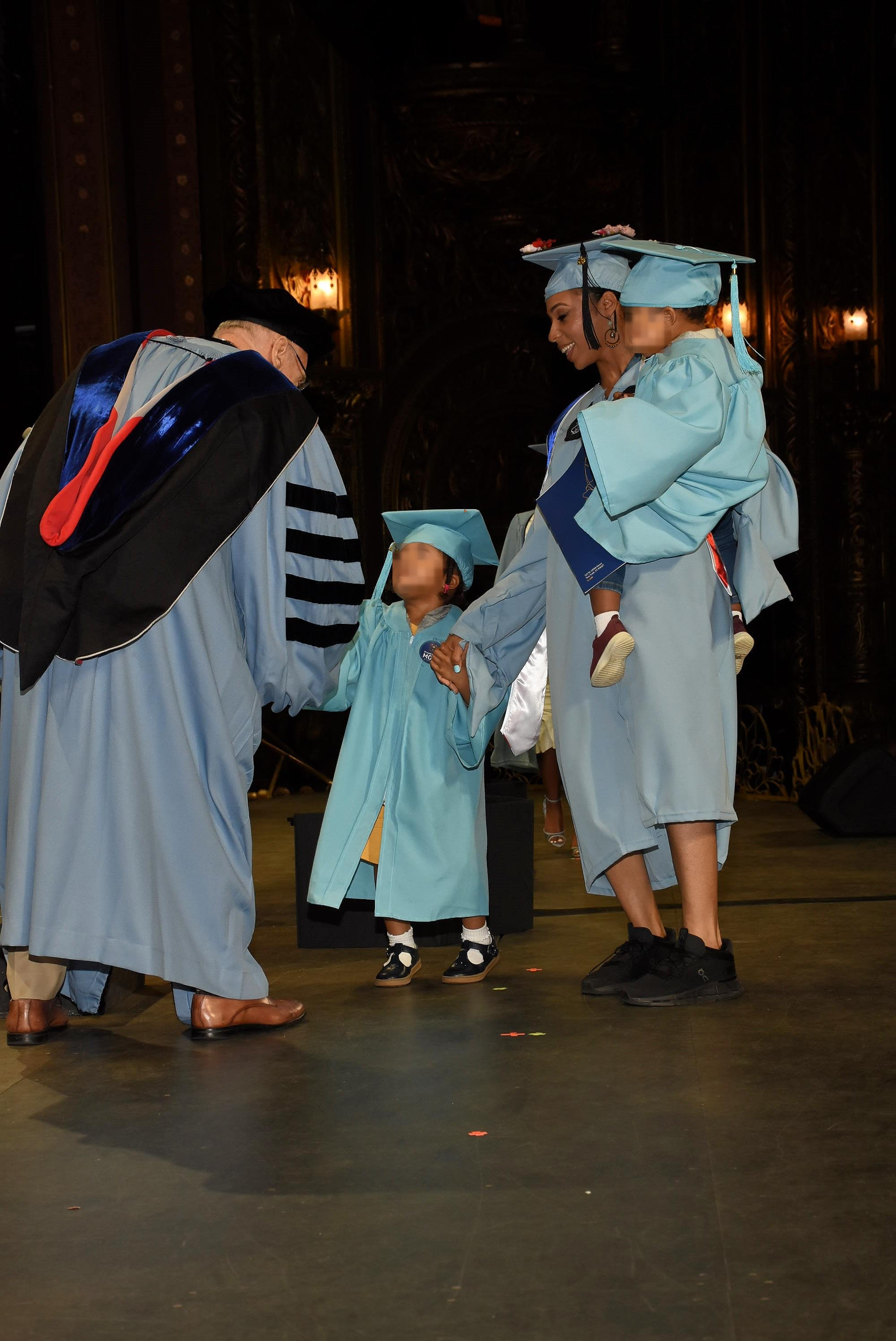 Janeica Davis walking across the stage at her Columbia University graduation with her two children, all in caps and gowns.