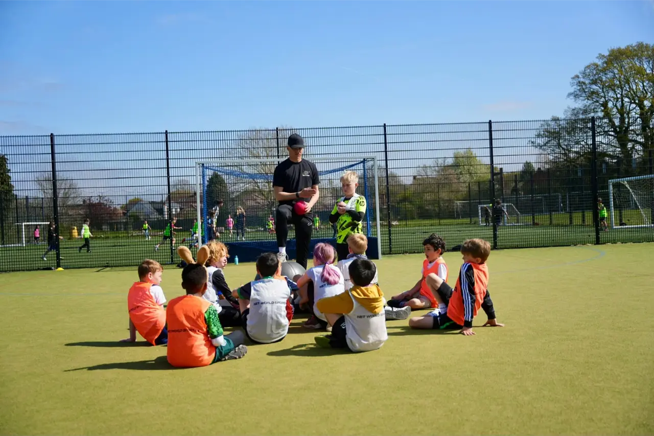 Coach leading a team sports training session with children seated on the pitch in Esher