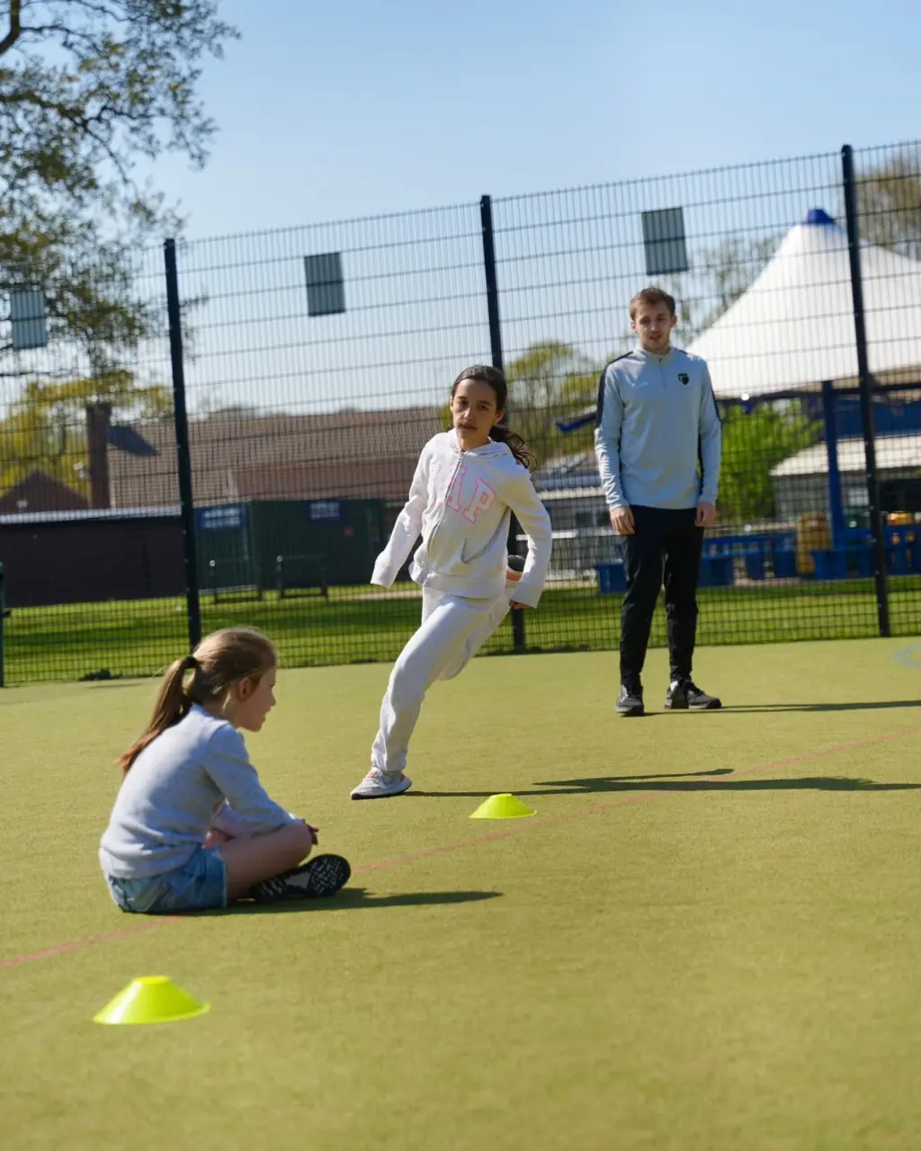 Girl practicing footwork and agility drill around cones with coach observing in Esher