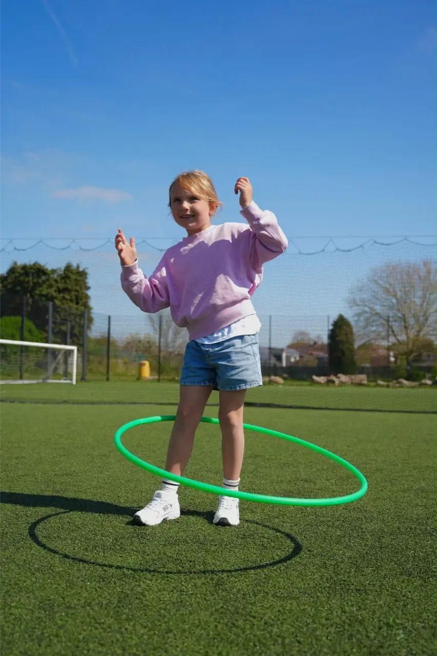 Young girl spinning a hula hoop on the sports pitch in Esher