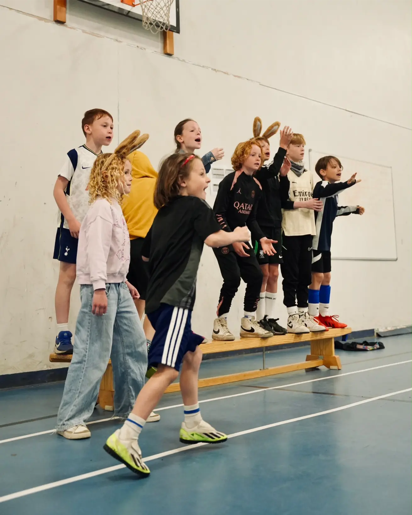 Group of excited children wearing bunny ears cheering together from a bench during holiday camp games in Esher