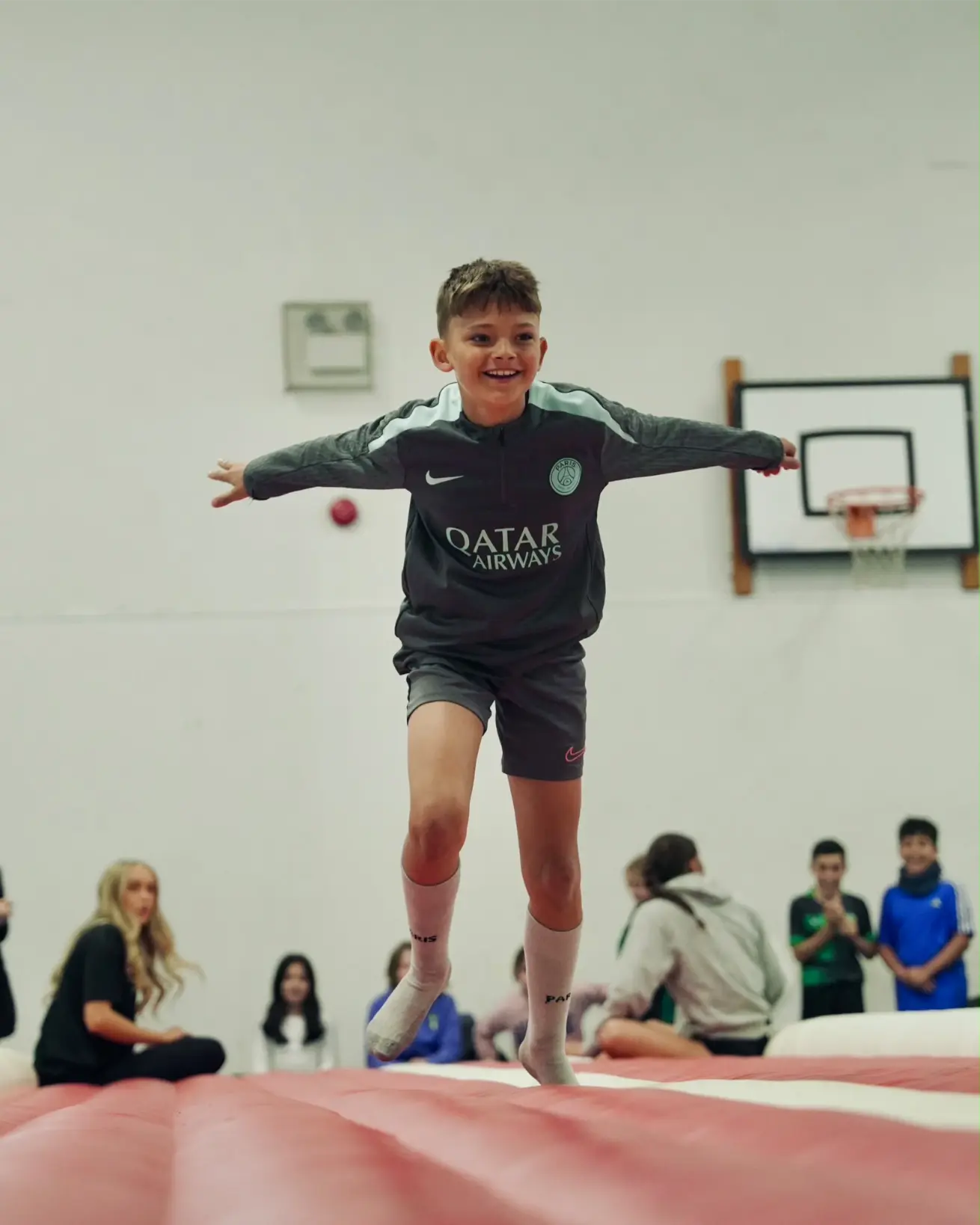 Young boy smiling and leaping with arms outstretched on an inflatable tumble track during a sports camp in Esher