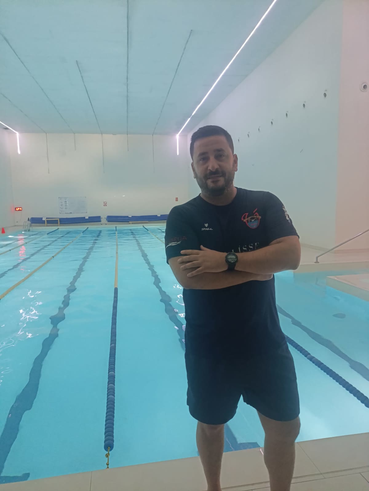 Alfonso con los brazos cruzados y camiseta del club junto a la piscina