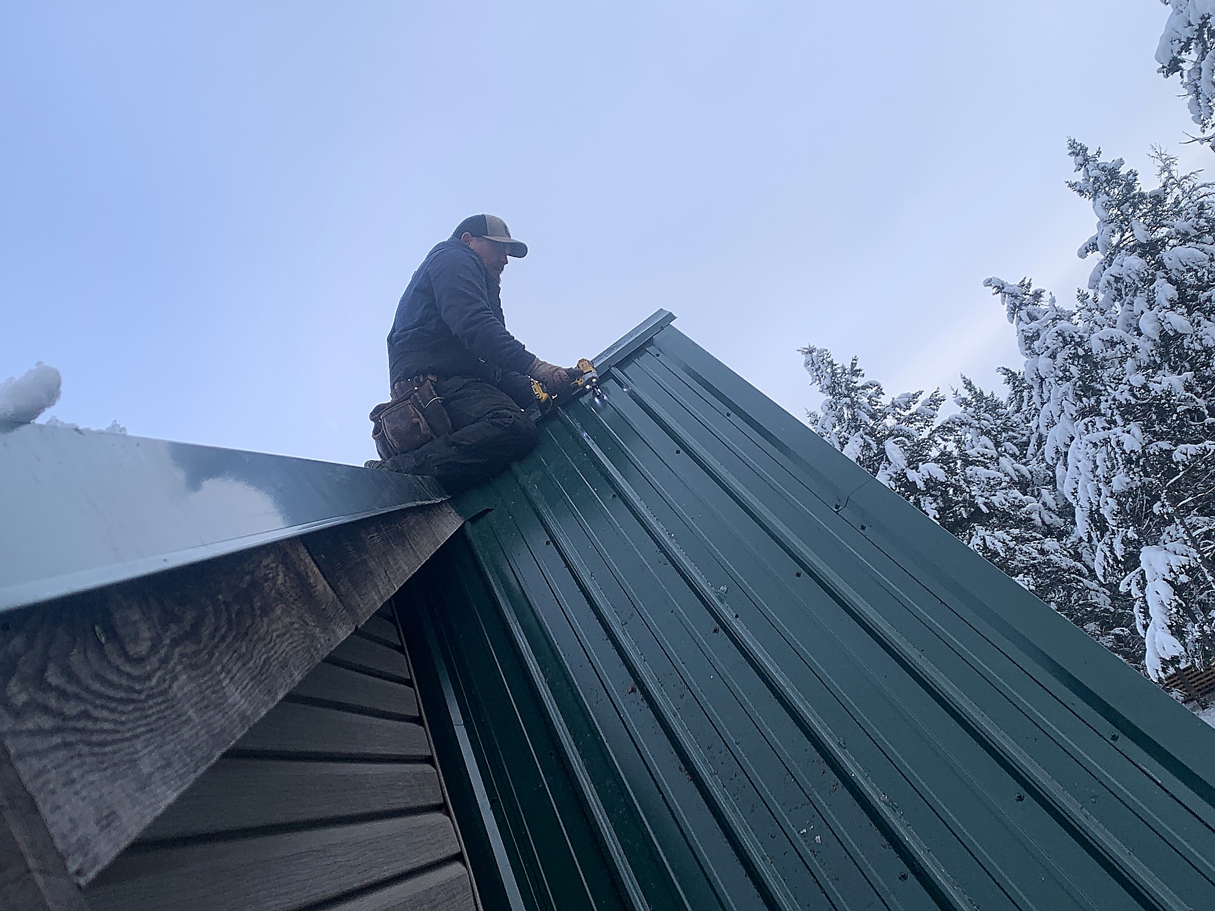 Flathead Valley Roofing crew member fastening green metal roofing in winter, Montana