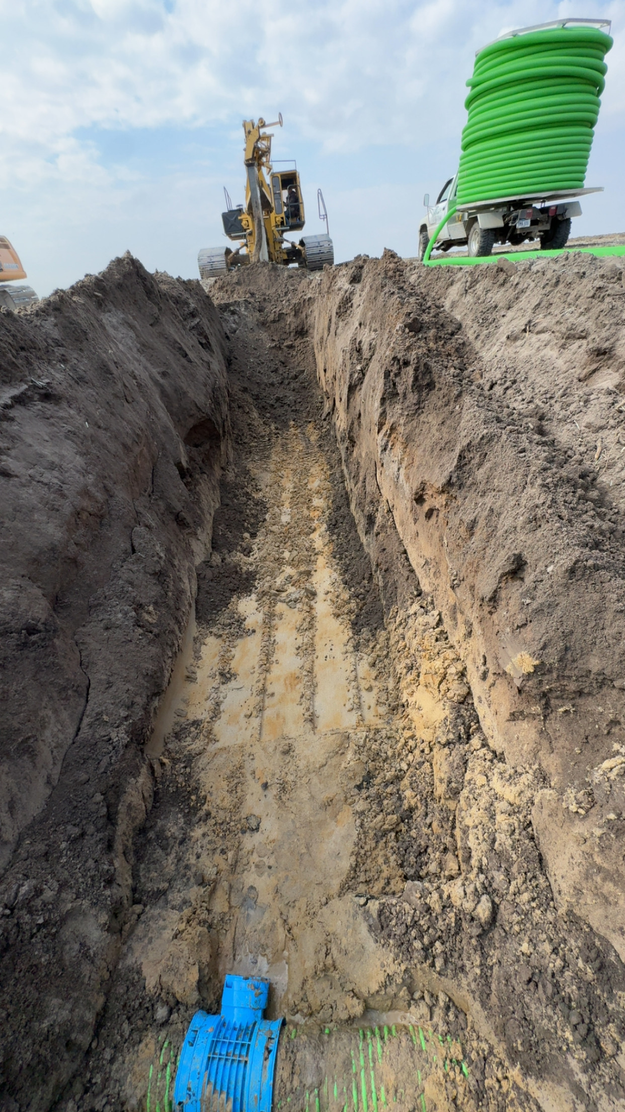 Deep trench excavation and underground utility pipe installation with equipment on site.