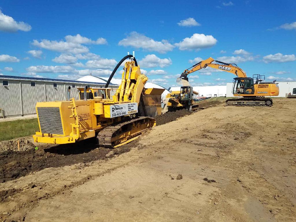 Heavy tiling plow and excavator installing farm tile drainage across Iowa ground.