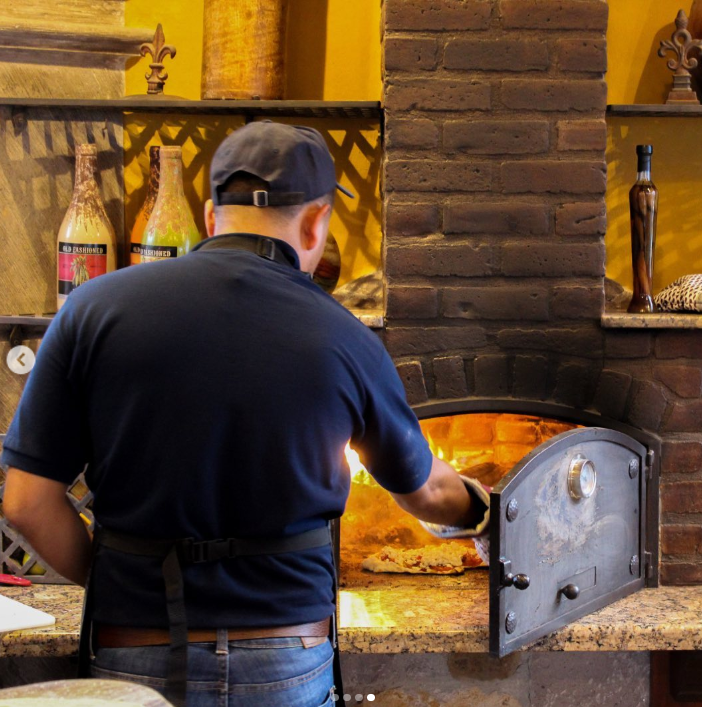 Chef baking fresh artisan pizza inside the authentic brick wood-fired oven at Casa Grande