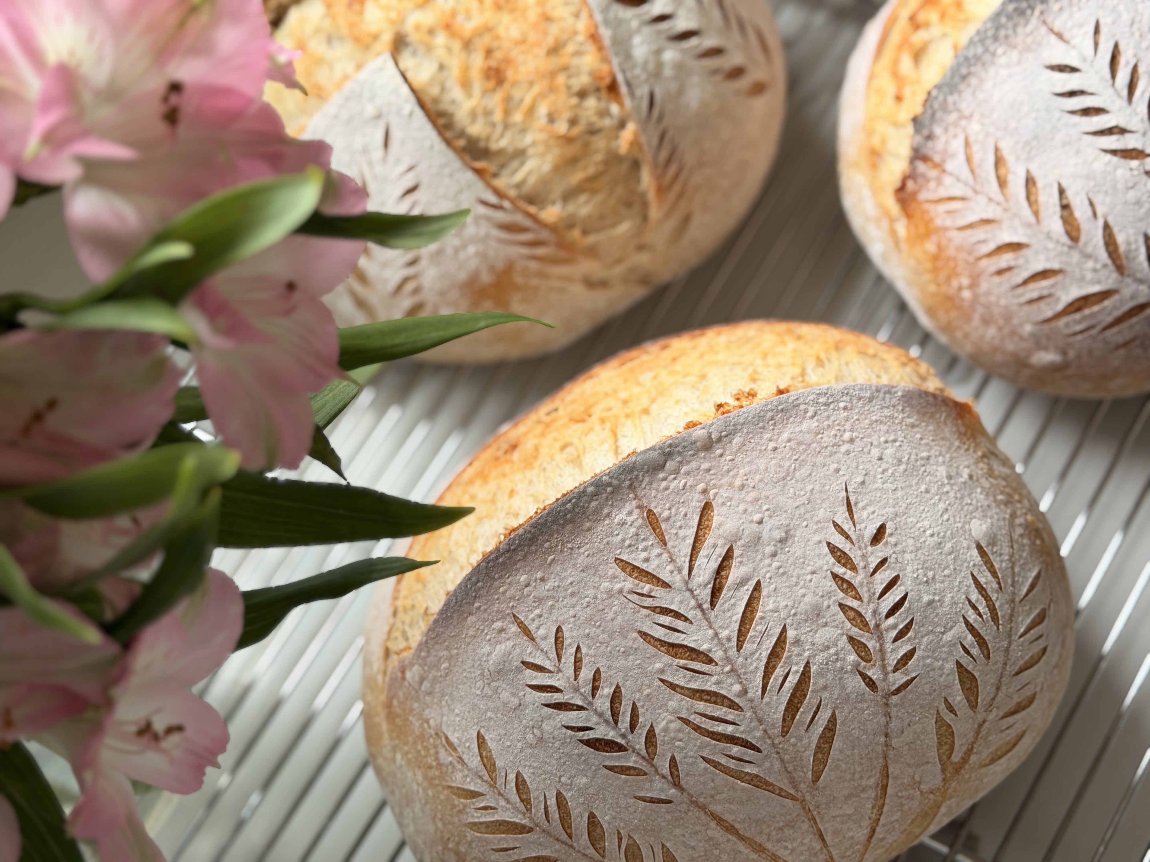 Freshly baked artisan sourdough loaves with delicate wheat sprig scoring alongside spring flowers