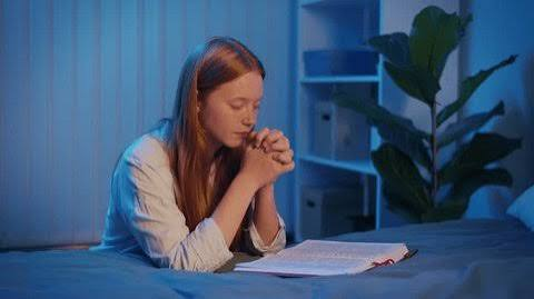Joven orando junto a la cama con la Biblia abierta