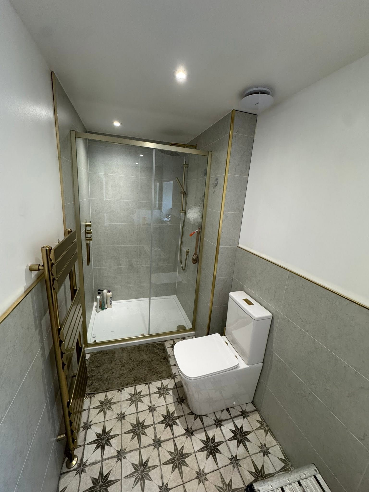 Walk-in shower renovation with gold brass fixtures and star patterned floor tiles by MMA All Trades Dundee