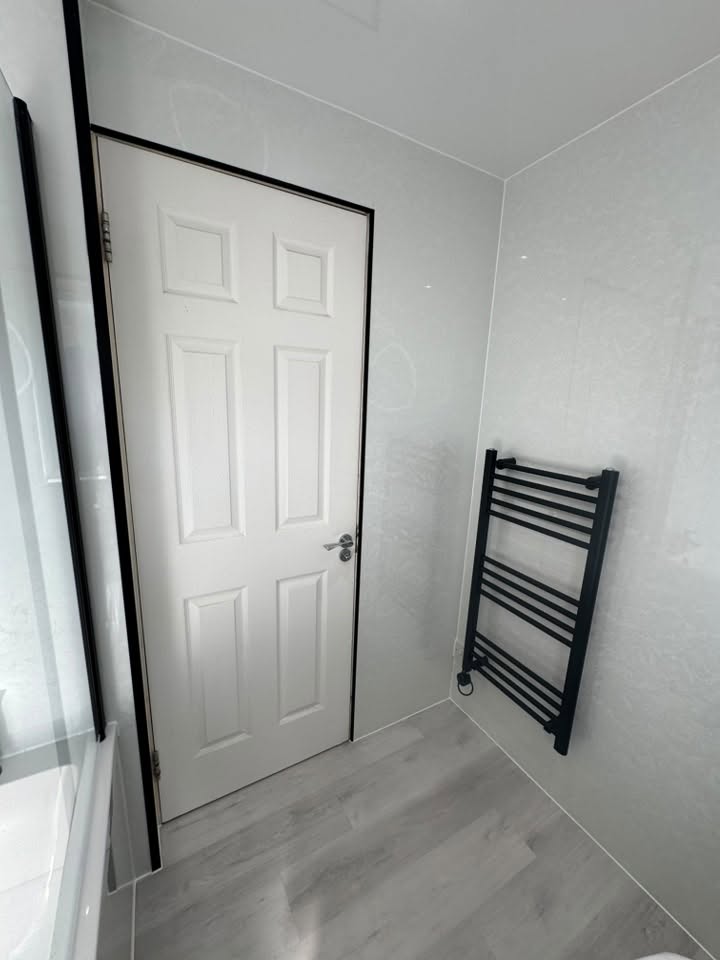 Crisp white wet-wall bathroom with matte black heated towel rail and grey flooring by MMA All Trades Dundee