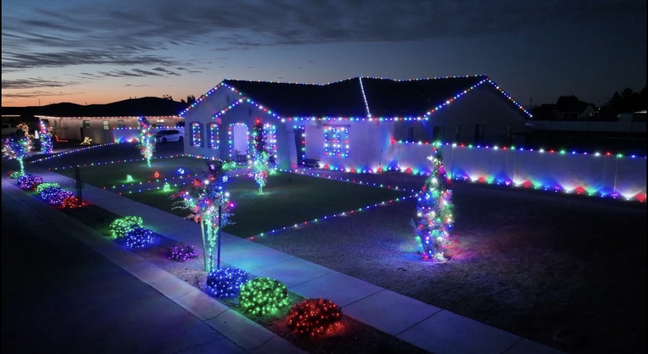 Vibrant multi-color commercial LED holiday lighting across roofline peaks, windows, walkway border, and illuminated trees