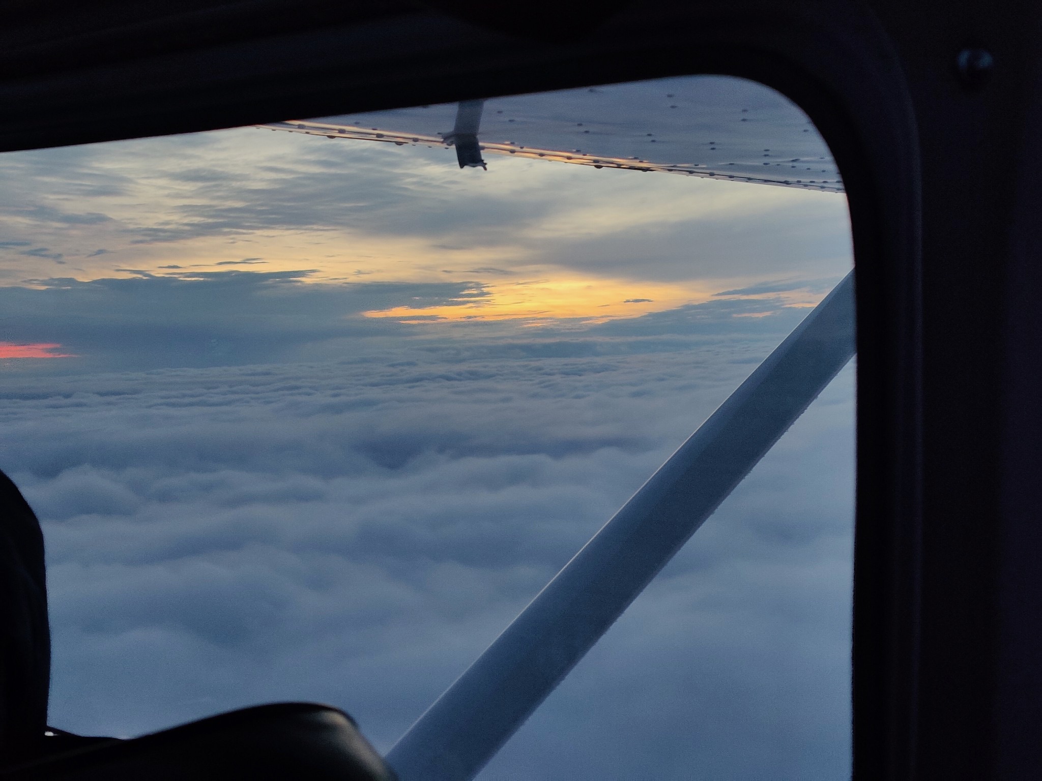 In-flight cockpit view through aircraft window above cloud layer at sunset