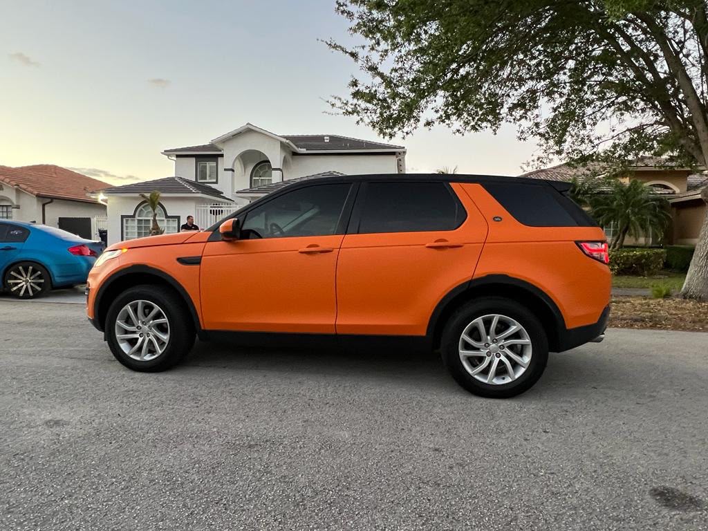 Side profile of Range Rover Discovery Sport wrapped in satin sunset orange with gloss black roof and pillar accents in South Florida