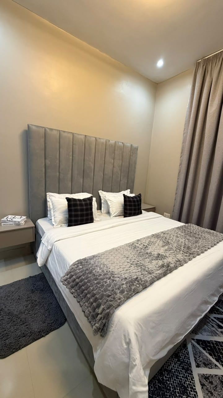 Master suite with tall grey vertical-channel padded headboard, crisp white bed linen, plaid accent pillows and plush textured throw