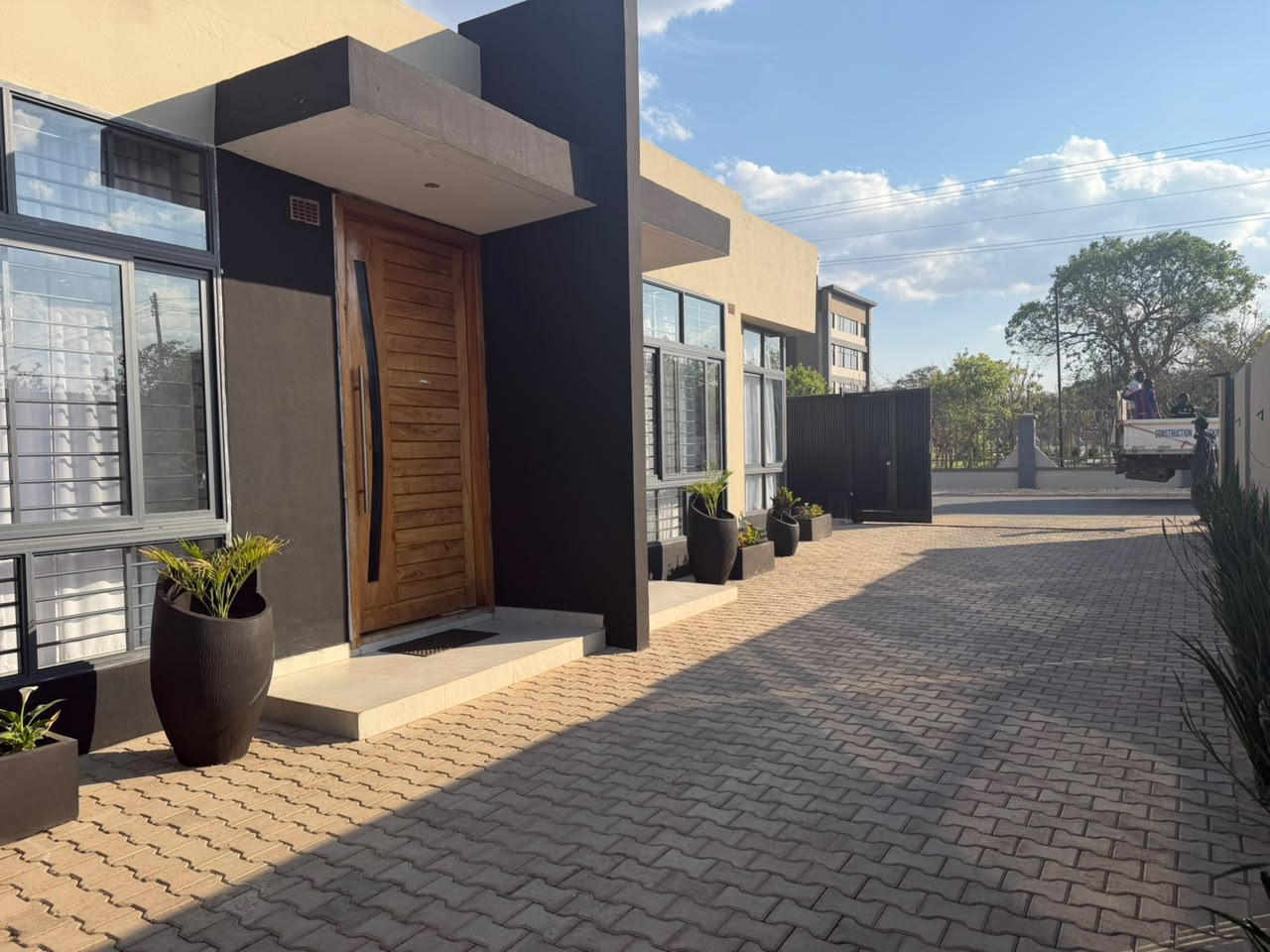 Modern apartment front entrance with timber pivot door, architectural planters and paved driveway