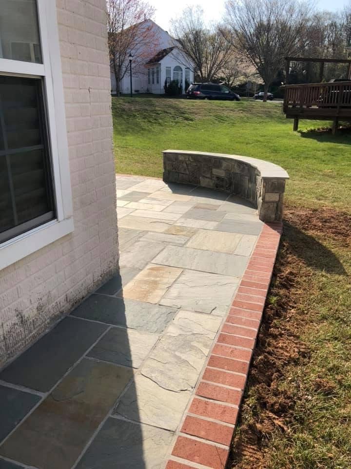 Natural stone patio paving with red brick border and curved low capped stone wall