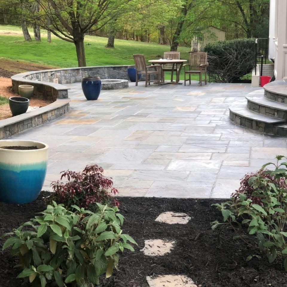 Natural stone patio with curved seating wall and rounded steps by Lionstone