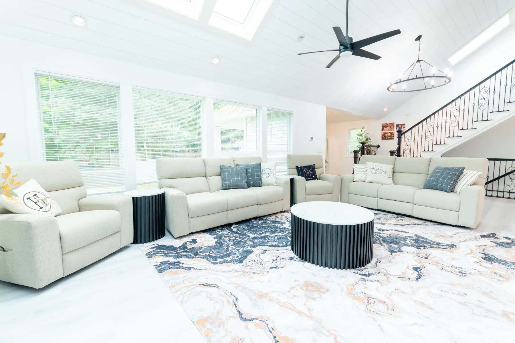 Bright, spacious living room with vaulted ceilings, large windows, modern furnishings, and an open staircase in a Southern Maine home.