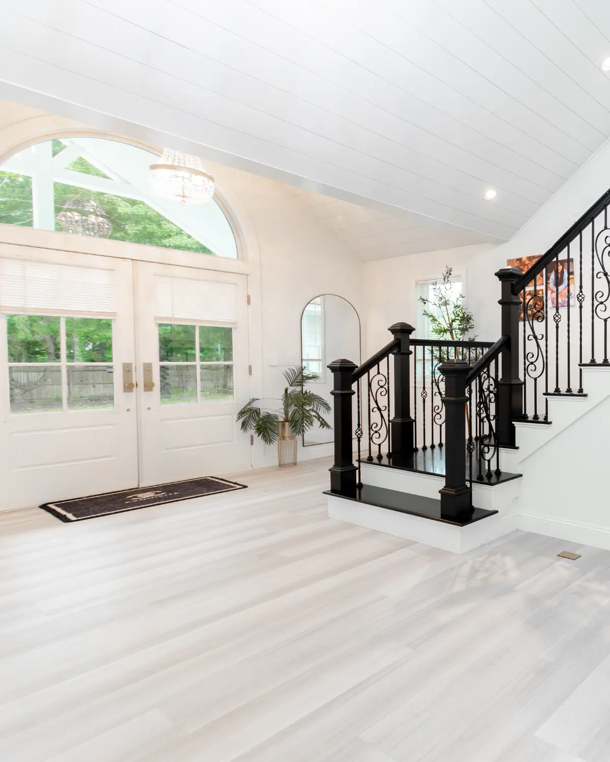 Bright residential entryway featuring an arched window, double doors, and elegant black staircase railing.