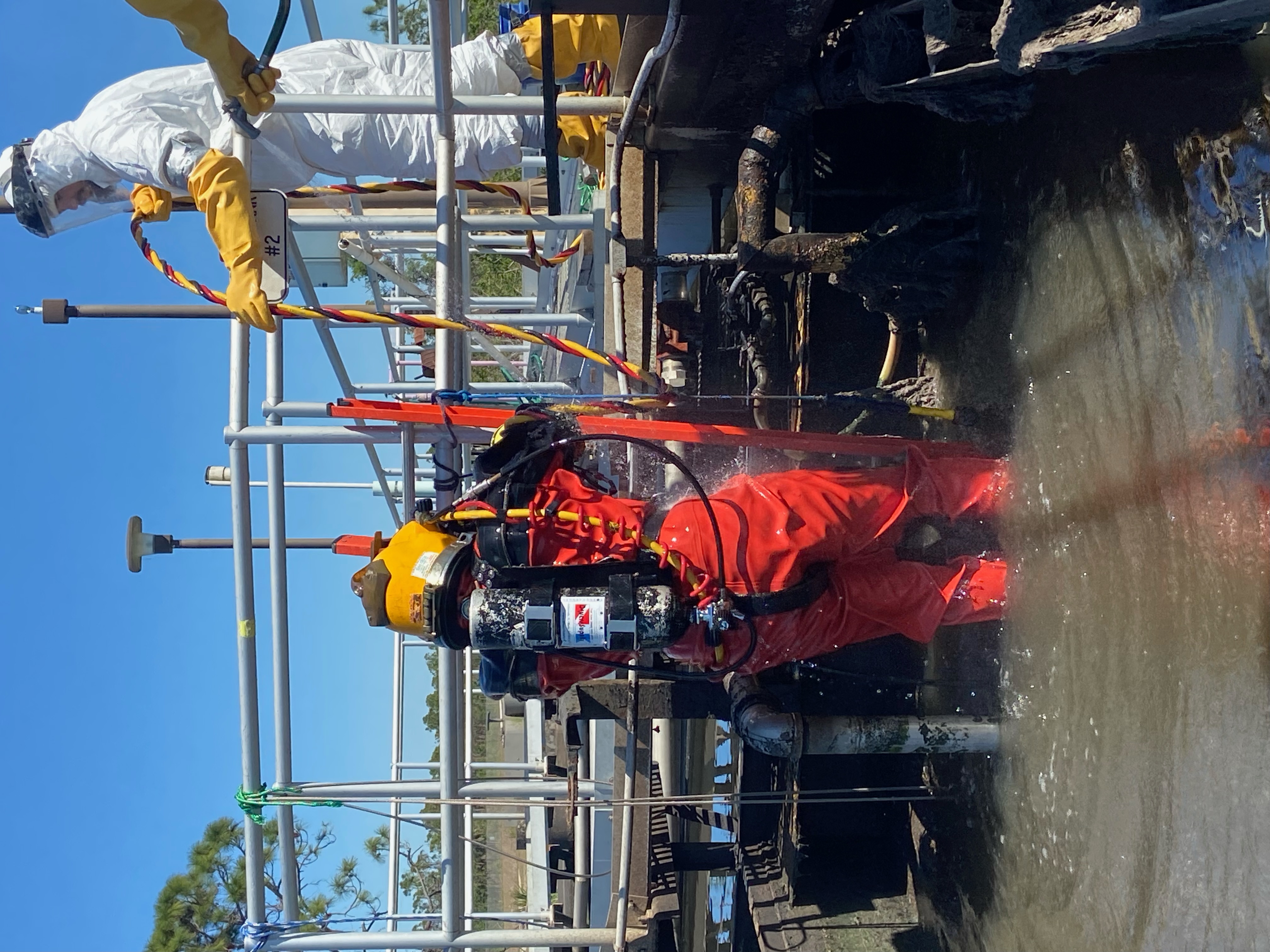 Diver in sealed gear in a wastewater tank with a decon tender.