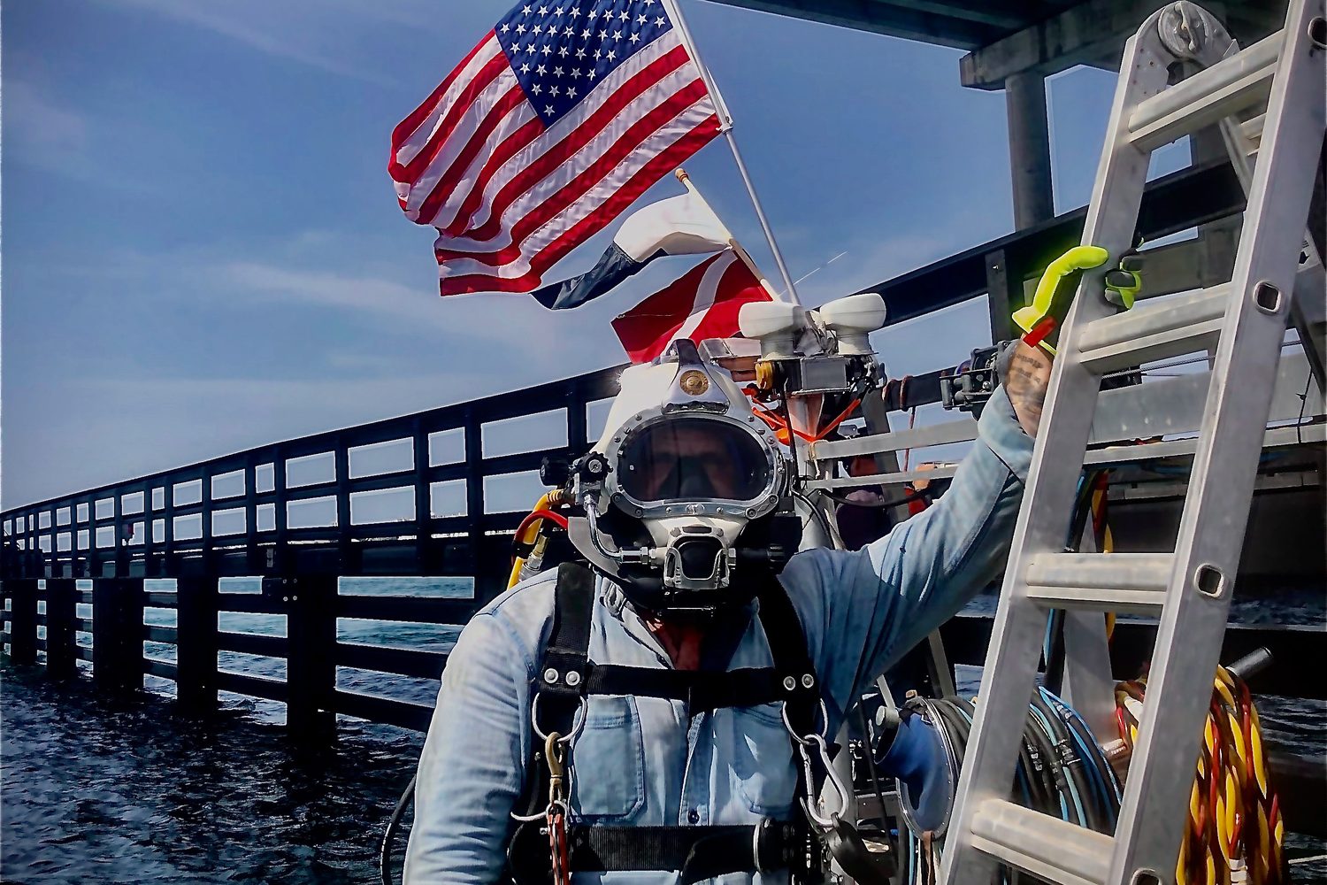 Commercial diver in a surface supplied helmet at a pier, ready for an emergency response dive.