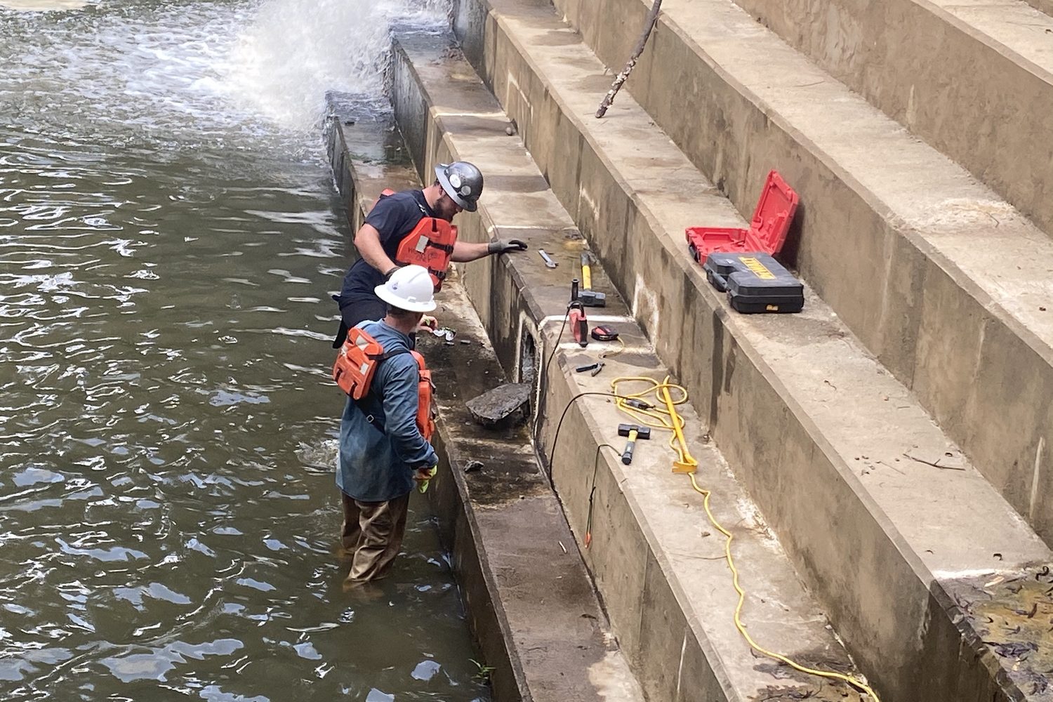 Crew with tools at a spillway stair apron.