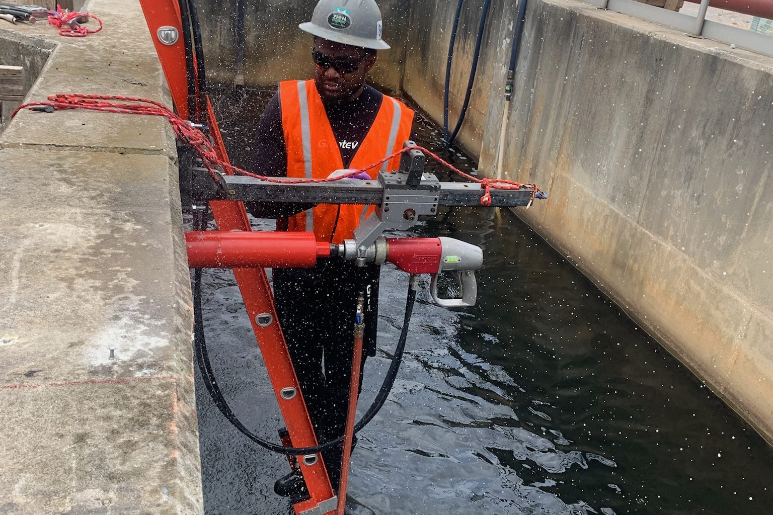 Crew member using a hydraulic drill in a wastewater channel.