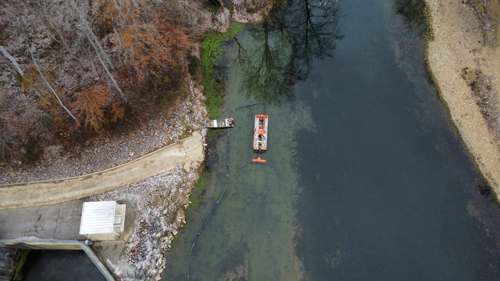 Aerial view of a dredge working beside a dam outlet.