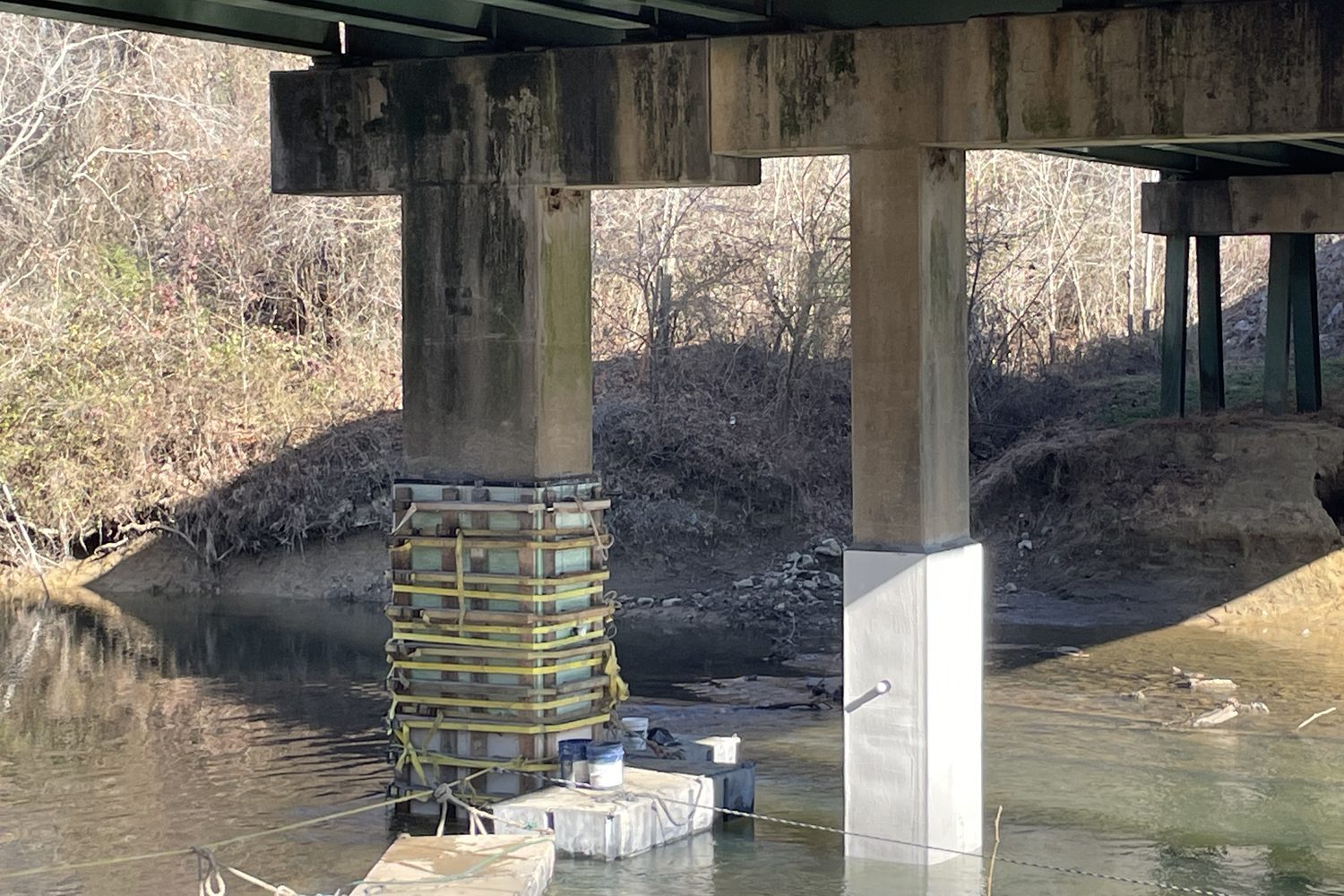 Bridge pier with a jacket form in place next to a finished white pile jacket.