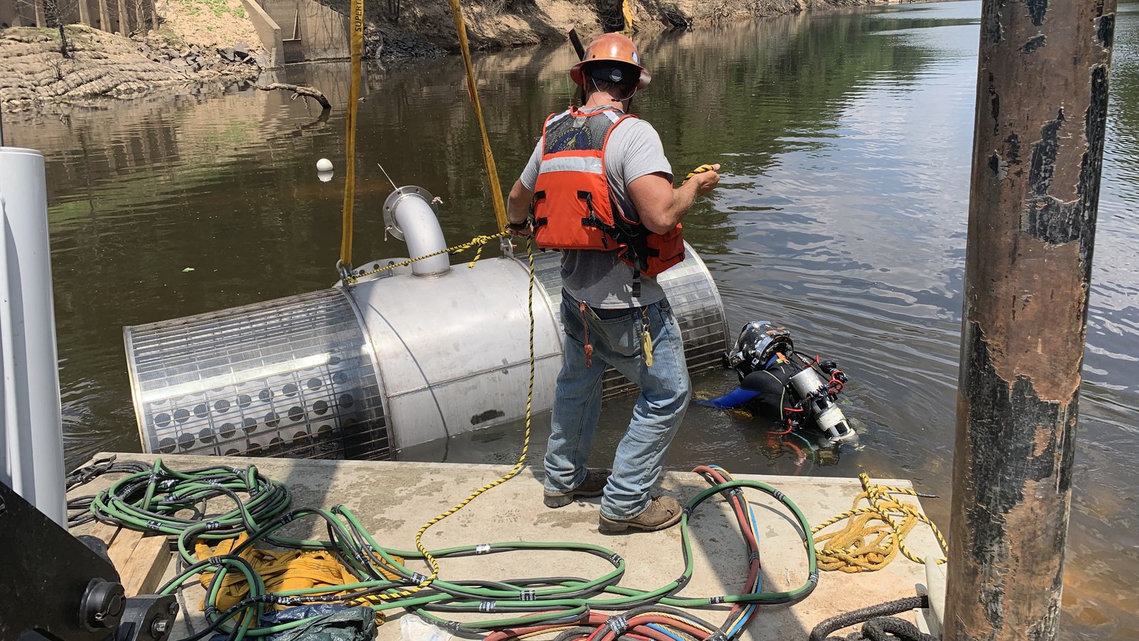 Tender and diver with an intake structure on a river bank.