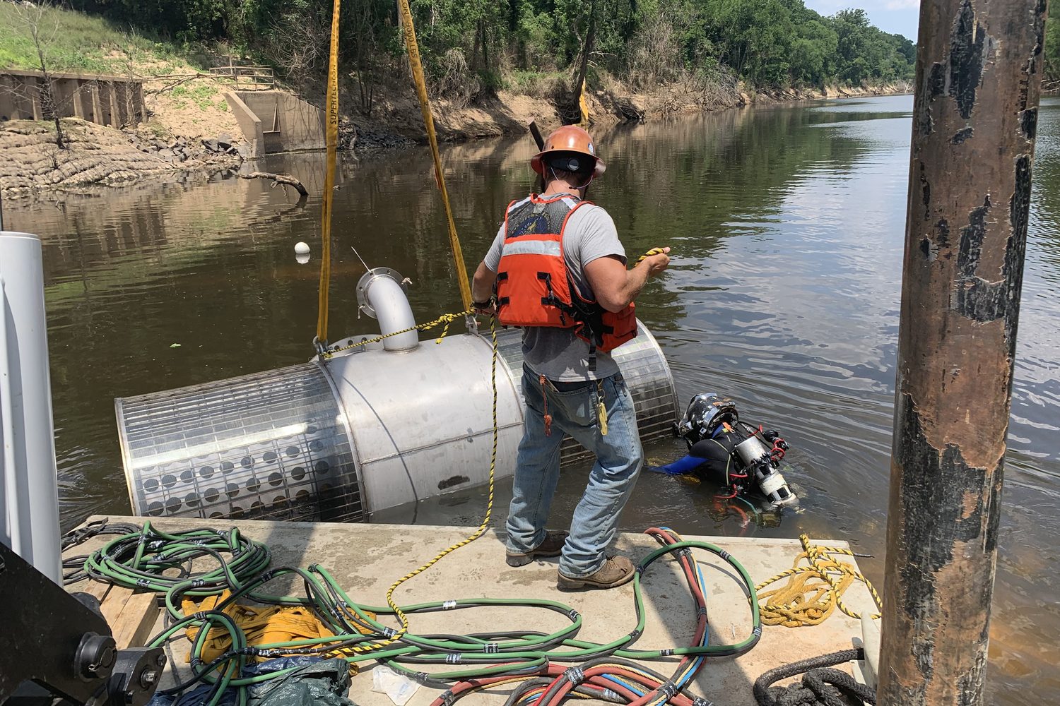 Diver and tender beside a screened intake on a work barge.
