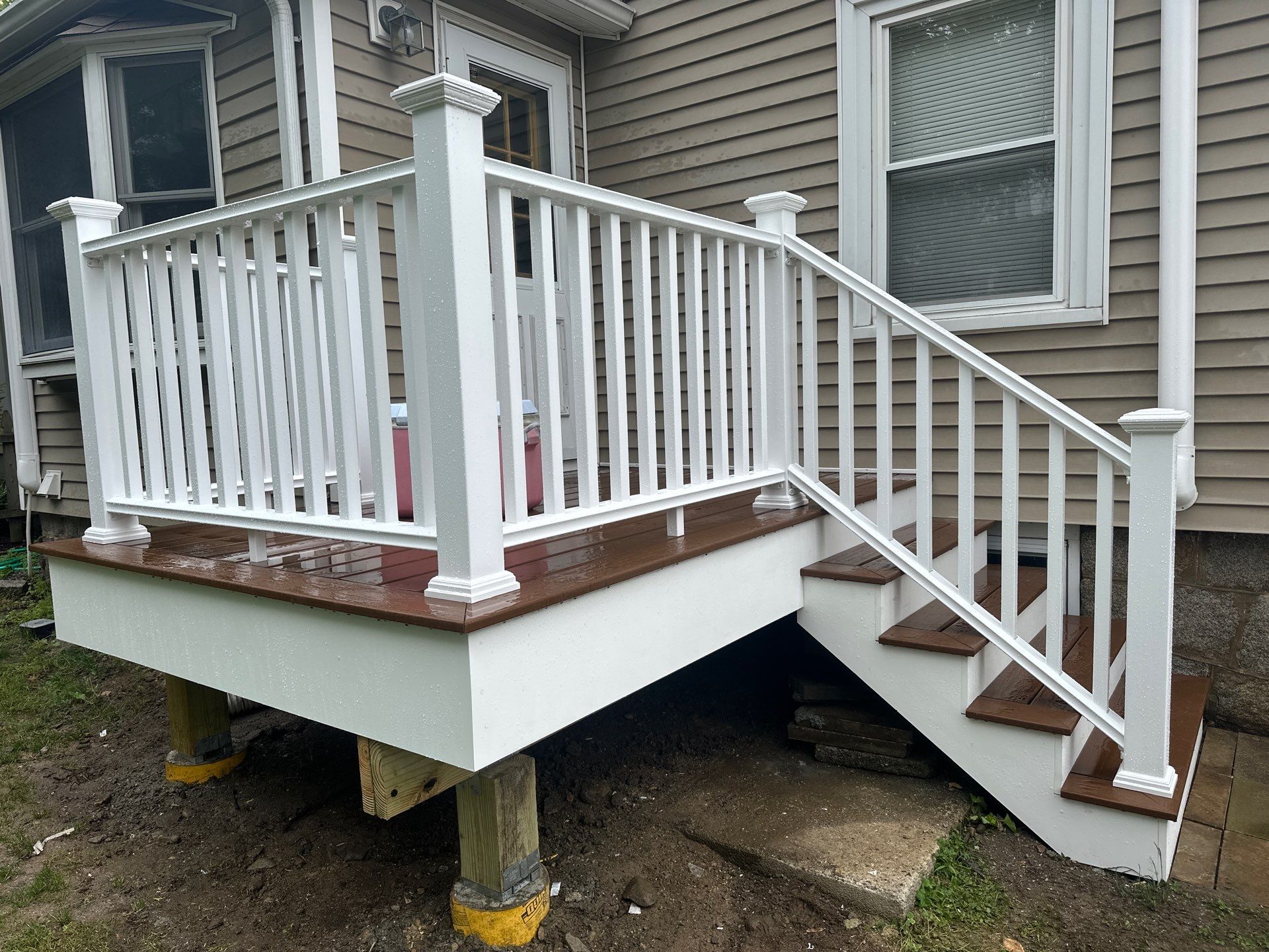 Custom entry deck and staircase with rich warm brown composite boards, white vinyl railings, and heavy-duty concrete footings