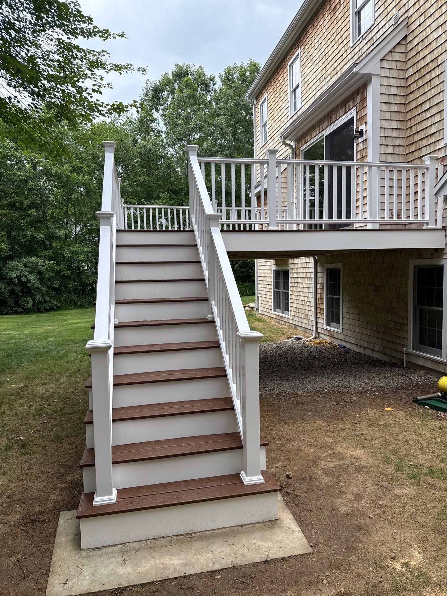 Straight-on view of custom elevated outdoor staircase with two-tone brown composite treads and white railings leading to second story deck