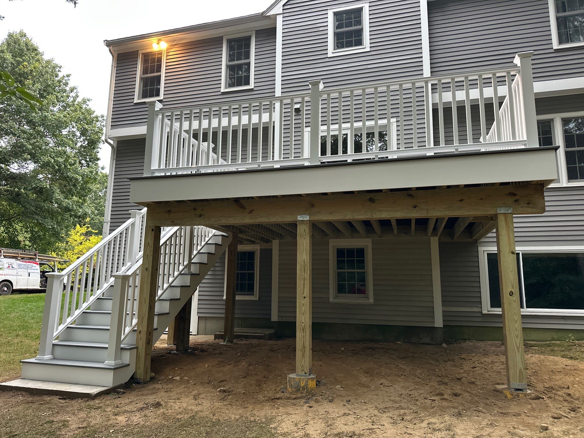 Raised two-story custom deck with white vinyl railings, wide open staircase, structural posts, and grey trim on a Massachusetts home